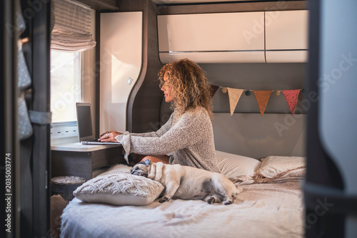Foto Woman working on a laptop inside a cozy camper van while her pug sleeps on the bed, capturing remote work, travel lifestyle and relaxed, homey comfort in a compact motorhome interior