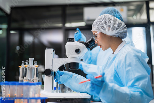 Konstfotografi Asian female scientist team in cleanroom suit using microscope for medical research in laboratory