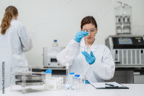 фотографія Professional female scientist stirring liquid sample in beaker with glass rod at modern laboratory