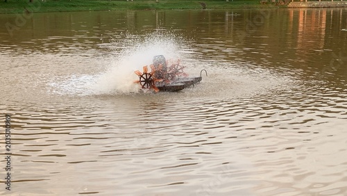 Foto Mechanical paddlewheel aerator splashing muddy pond water, creating ripples and