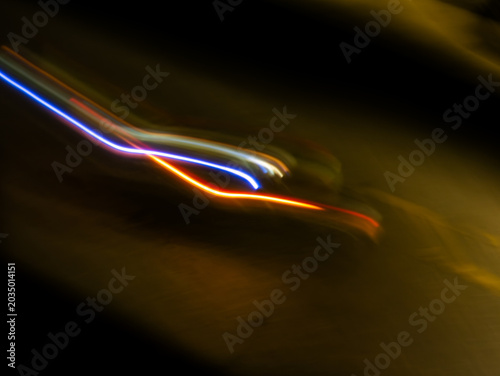 Abstract long exposure light trails with blue white and orange red streak crossing on dark black background at night street