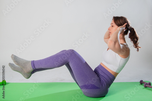Full length portrait of young woman in sportswear doing abdominal exercise on yoga mat isolated on white background.