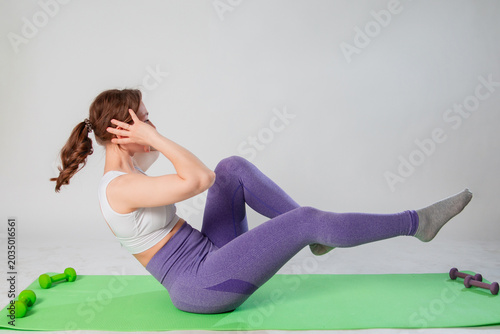 Full length portrait of young woman in sportswear doing abdominal exercise on yoga mat isolated on white background.