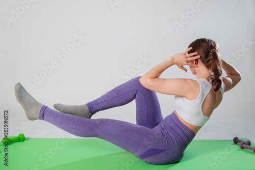 Full length portrait of young woman in sportswear doing abdominal exercise on yoga mat isolated on white background.
