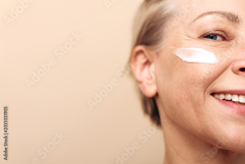 Foto Close-up of smiling middle aged woman with cream on cheek against beige background