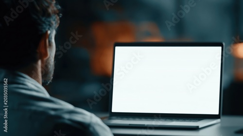 Over the Shoulder View of a Man Using Laptop with Blank White Screen at Night