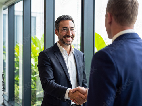 Photos Smiling businessman with glasses shaking hands with a colleague, symbolizing successful partnership