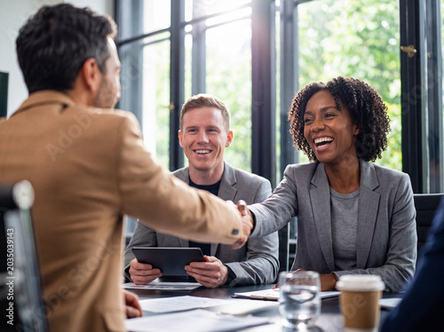 Fotografie Happy diverse business partners shaking hands after a successful meeting in a sunlit modern office setting