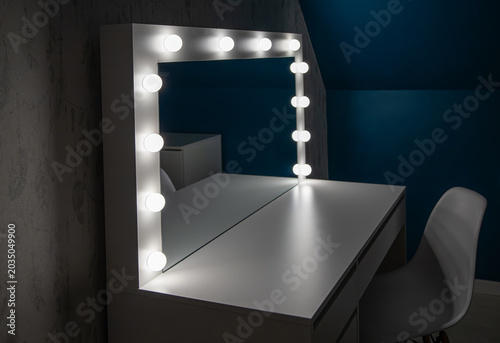 White modern vanity table with light bulbs illuminated in a dark room in home blue color wall bedroom.