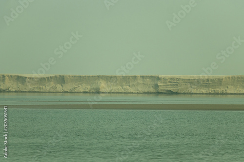 A massive white sandy cliff rises over a calm riverscape