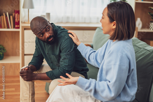 Fotografía Multiracial couple sitting on sofa at home and arguing