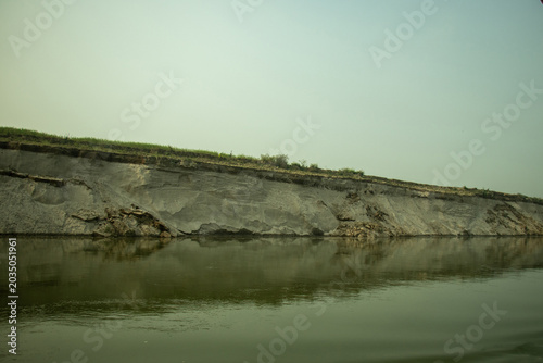 A severely eroded grey clay cliff actively collapsing into a murky