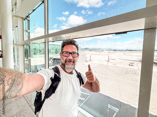 Εκτύπωση καμβά Man taking a cheerful selfie at an airport terminal with backpack, giving thumbs