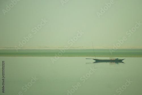 A weathered wooden fishing boat rests on a glassy river shore