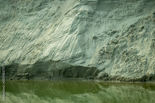 Extreme closeup of an eroded pale grey sediment cliff face, with deep