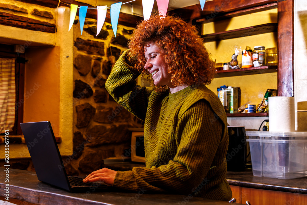 Obraz premium Redhead woman laughing while working on laptop, enjoying remote connection from rustic home