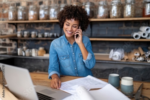 The woman running a small creative studio smiling while working on laptop and phone