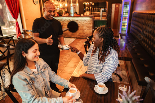 Woman making contactless payment to waiter at cafe