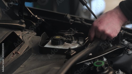 Unplugging a connector under the hood of a car. Close up hands and engine compartment.