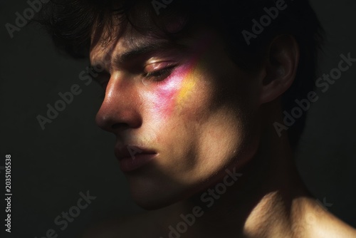 Male side portrait with iridescent magenta and yellow light on cheek for artistic beauty background and moody editorial design