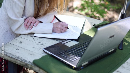 Slow motion 4k video of a female hands of a writer works in front of a laptop monitor in a city park. Runaway from the confines of a stuffy office in a noisy city.