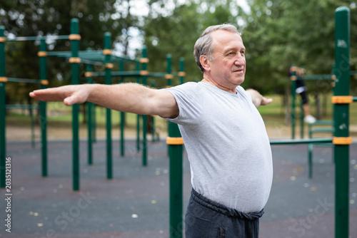 Vászonkép elderly man does gymnastics on an outdoor sports ground