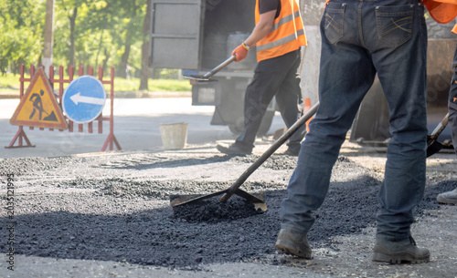 Bild auf Leinwand Road construction worker using a rake to level fresh asphalt with warning traffi