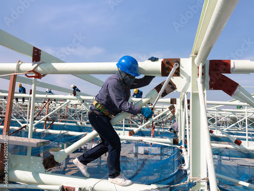 Construction worker uses torque wrench to tighten bolts on metal structure. Industrial engineering scene highlights structural steel assembly, workplace safety and precision construction techniques.