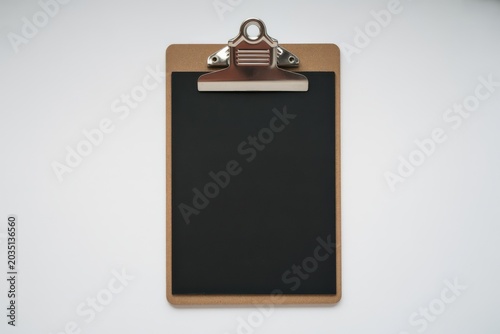 A brown clipboard with a black board and metal clip is shown on a gray background