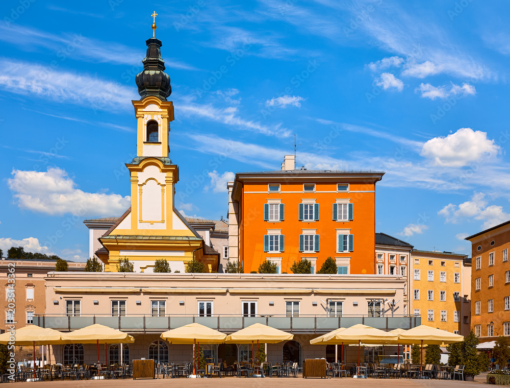 Obraz premium Salzburg, Austria. Chapel tower and street cafe of the central square of the historic old town among old austrian buildings architecture. Sunny summer day. Blue sky with clouds.