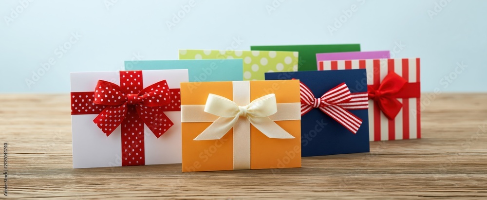 Fototapeta premium Colorful gift cards with festive ribbons on wooden table for holiday shopping and gift giving.