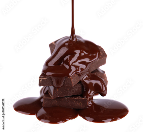 Liquid chocolate syrup pouring over a stack of chocolate pieces isolated on a white background. Clipping path.