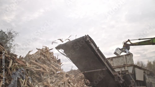 Landfill. Excavator belt wood chipper. Wood processing. Recycling. Ecology. Large mountains of bulk wood biomass. Wood recycling and processing.