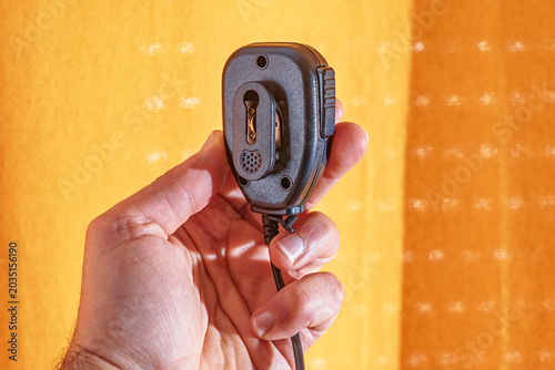 PTT, secure microphone in white man's hand on yellow fabric surface in backlight.