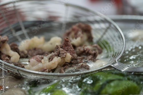 Canvastavla colander scooping freshly blanched fresh beef for hot pot