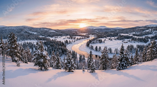 Panoramic landscape view of a winding river flowing through a serene snow covered forest during a beautiful winter sunset light
