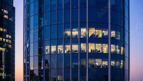 Fotografie Modern glass office tower at dusk with interior lights business district buildin