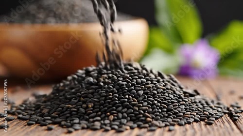 Black sesame seeds pouring onto a rustic wooden table.