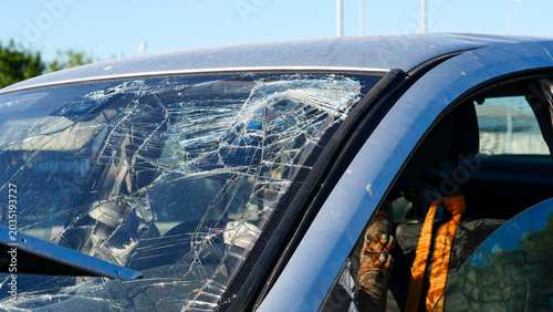 Silver passenger car after a traffic collision on a city street. Damaged automobile with crushed bodywork and broken parts left outdoors on a public road after a vehicle accident or crash.
