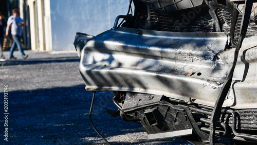Silver passenger car after a traffic collision on a city street. Damaged automobile with crushed bodywork and broken parts left outdoors on a public road after a vehicle accident or crash.