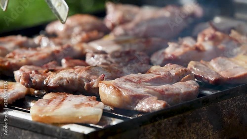 Meat preparing on barbeque close up, man turn pieces with tongs, fat sizzling and smoke rises