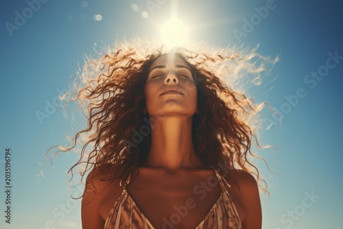 Young woman with closed eyes soaking up sun rays under clear blue sky, experiencing serenity