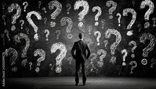 Man in suit stands before a wall covered in chalk question marks