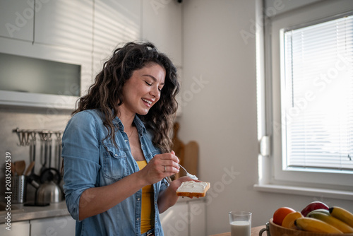 Fotografie Happy woman spreading cream cheese on toast for breakfast