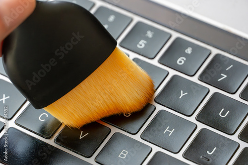 Soft detailing brush cleaning dust and debris from between laptop keyboard keys. Computer maintenance and electronics cleaning