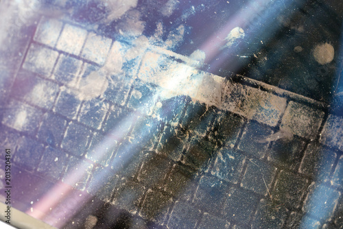 Abstract close-up of a dirty laptop screen with visible keyboard imprints, fingerprints, dust, and smudges reflecting light on a glossy display surface.