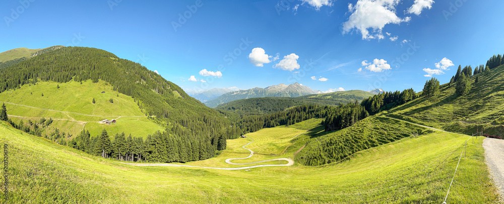 Fototapeta premium Panoramic View Of Green Mountains And Meadows Under Blue Sky In Königsleiten Austria Tirol During Summer Season For Travel And Tourism