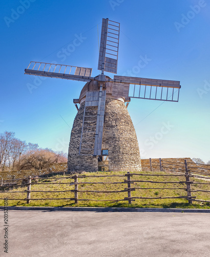 An antique windmill with a stone base and wooden blades, surrounded by a rustic fence.