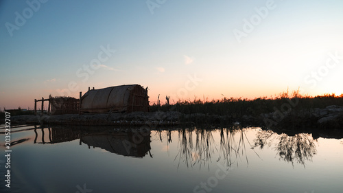Canvastavla Sunset over tranquil Iraqi Marshes with traditional homes by the water