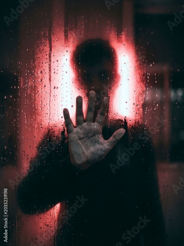 Silhouette of a hand on wet glass, red neon glow background.